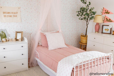 A twin bed made with woven pink zipper bedding and an assortment of pink pattern pillows and matching floral blanket.