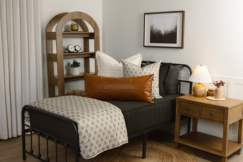A twin bed with black knit bedding with white, floral, and leather accessories. 