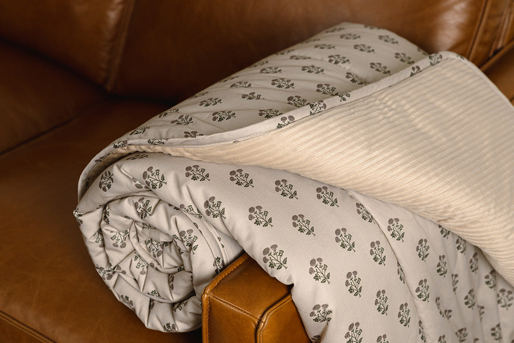 A tan, pink, and green blockprint floral  with cream corduroy minky blanket on an orange leather couch.