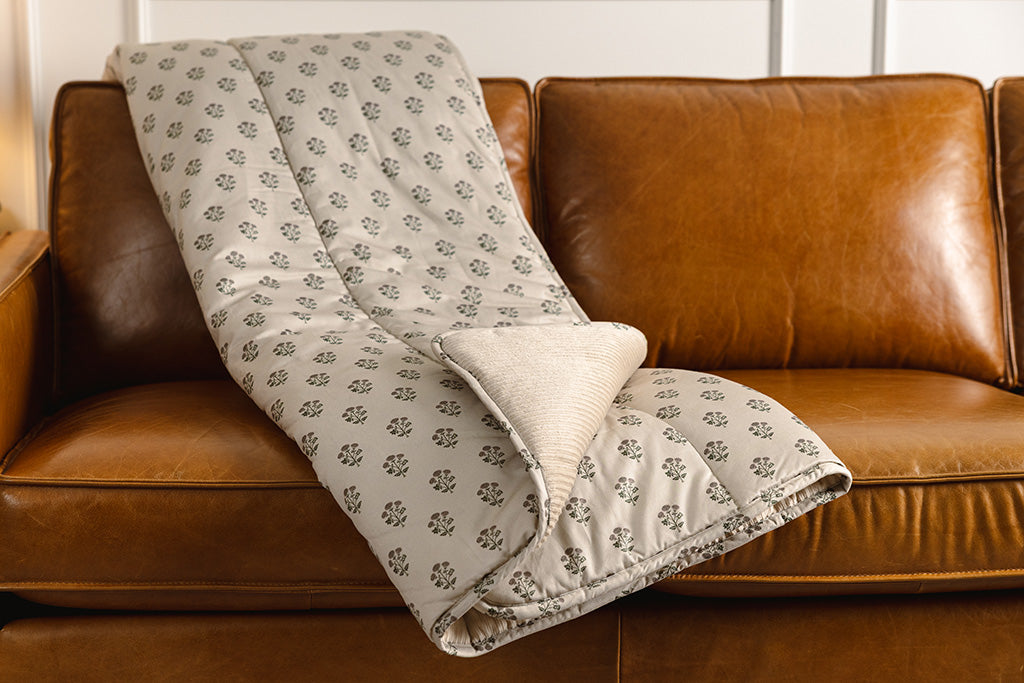 A tan, pink, and green blockprint floral  with cream corduroy minky blanket on an orange leather couch.
