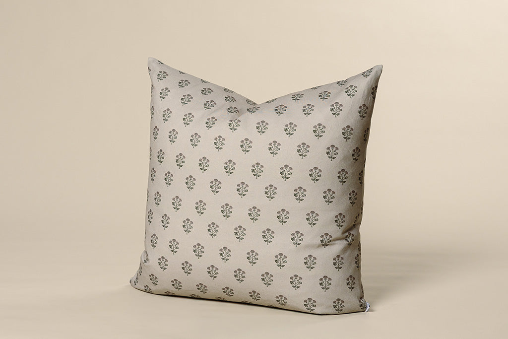 A tan, pink, and green blockprint floral pillow on a cream paper background.