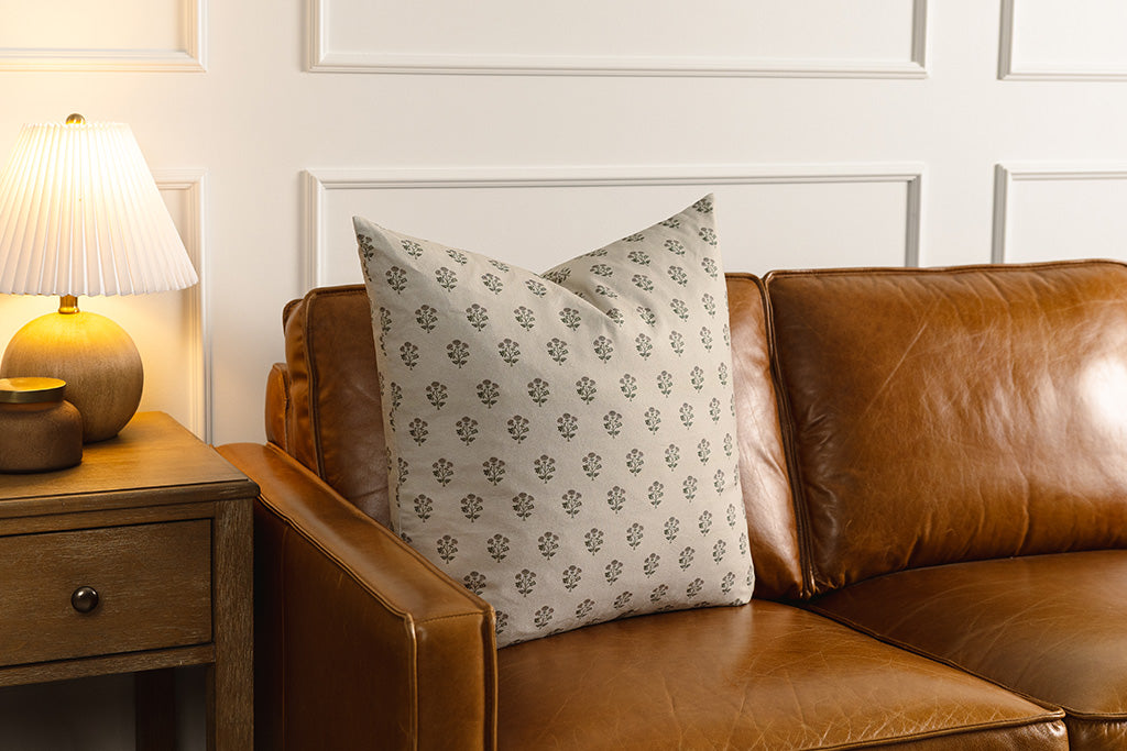 A tan, pink, and green blockprint floral pillow on a leather couch.