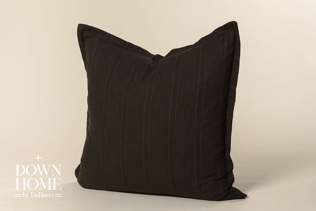 Black knitted pillow on cream background.