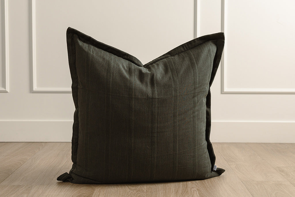 Black knitted pillow on wood floor and wainscoting background.