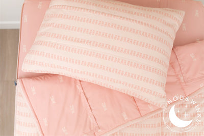 A twin bed made with pink ballet shoes kids zipper bedding, the top unzipped and slightly pulled back and a pillow on the bed.