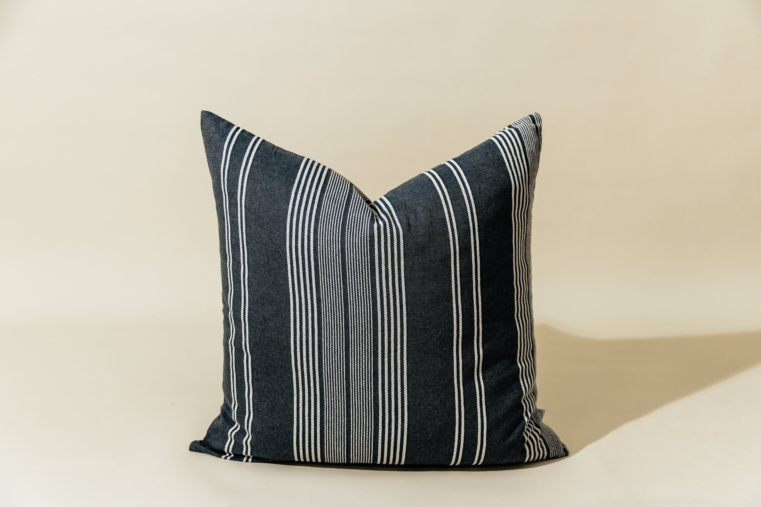 A woven dark gray and white striped euro pillow arranged on a cream background.