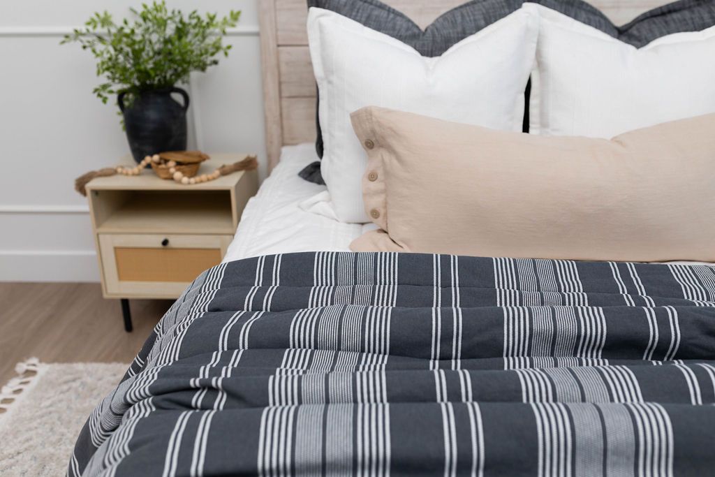 A close up of a bed made with white zipper bedding and neutral pillows and a charcoal gray striped blanket.