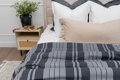 A close up of a bed made with white zipper bedding and neutral pillows and a charcoal gray striped blanket.