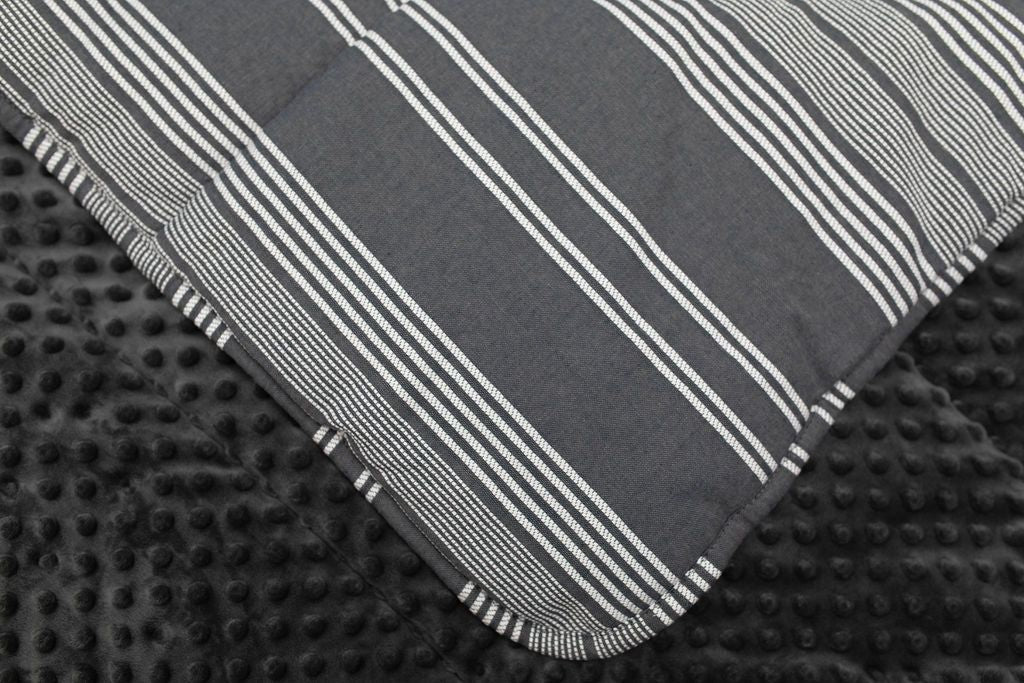 A close up view of a blanket folded revealing a softly textured dark gray minky and a white and gray striped pattern for the other side.
