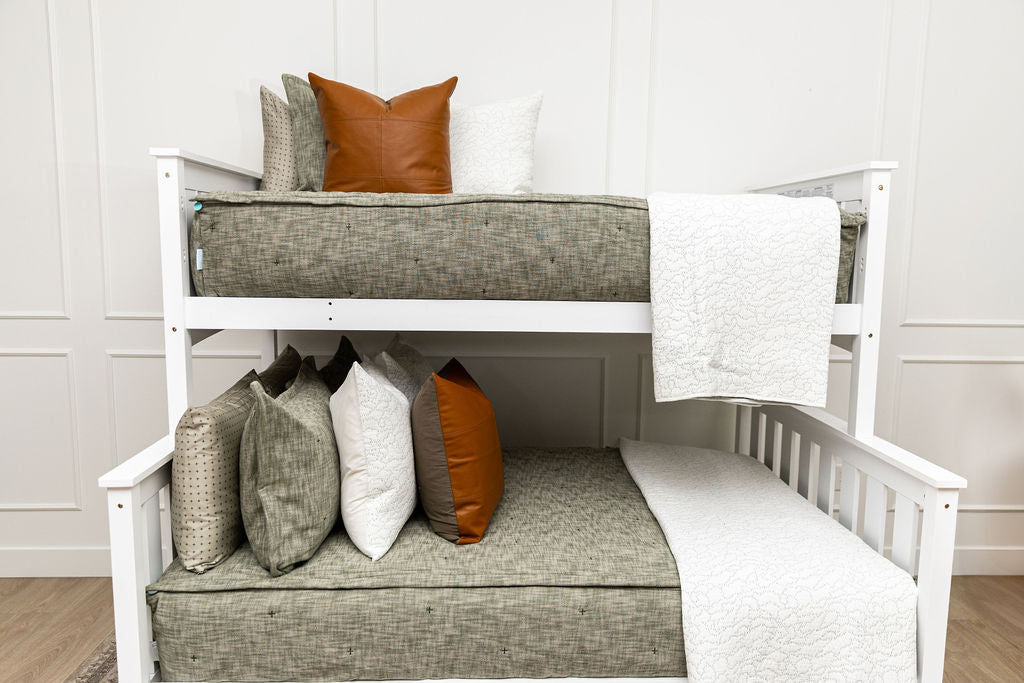 A standard bunk bed with both bunks made with deep emerald green zipper bedding and leather and white pillows and blankets.