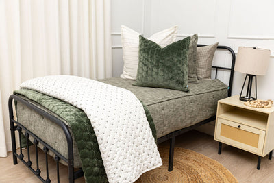 A twin bed made with deep emerald green zipper bedding and an assortment of white and velvet green pillows and blankets.