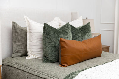 A close up view of a bed made with deep emerald green zipper bedding and neutral and green throw pillows and blankets.