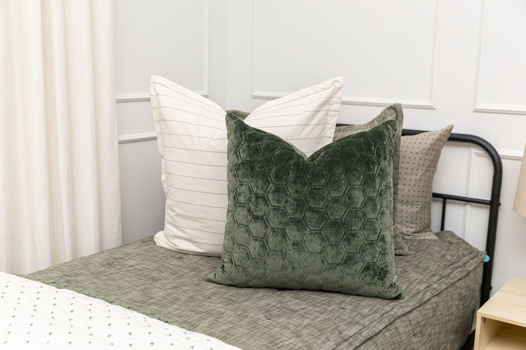 A close up view of a twin bed made with deep emerald green zipper bedding and an assortment of white and velvet green pillows and blankets.