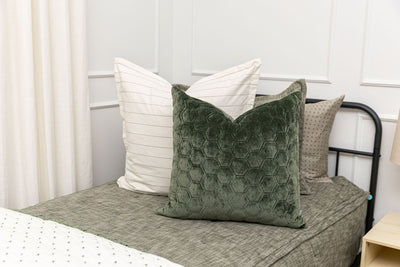 A close up view of a twin bed made with deep emerald green zipper bedding and an assortment of white and velvet green pillows and blankets.