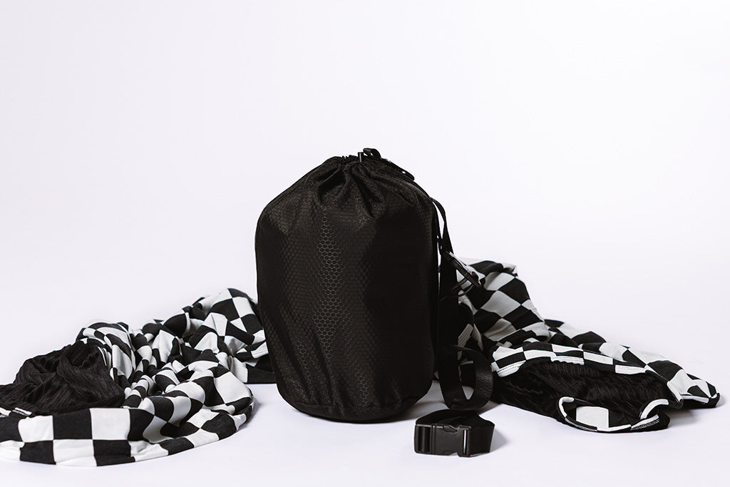 A black bag next to a black and white checkered blanket on a white backdrop.
