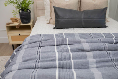 A close up of a bed made with cream embroidered zipper bedding adorned with neutral pillows and a blue striped pattern blanket.