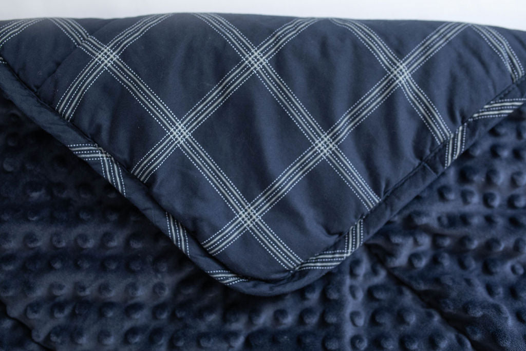 A navy blue plaid mini blanket folded over to reveal the minky interior.