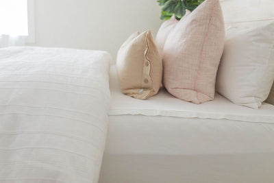 A side view of a bed made with white zipper sheets and a white woven textured zipper duvet folded half way down the bed and adorned with neutral and light pink pillows.
