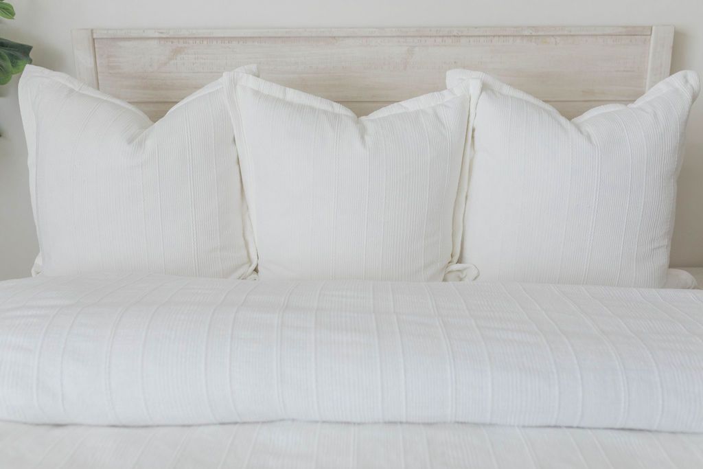A view of a bed made with a white textured zipper duvet as well as some matching large pillows.