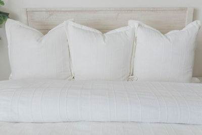 A view of a bed made with a white textured zipper duvet as well as some matching large pillows.
