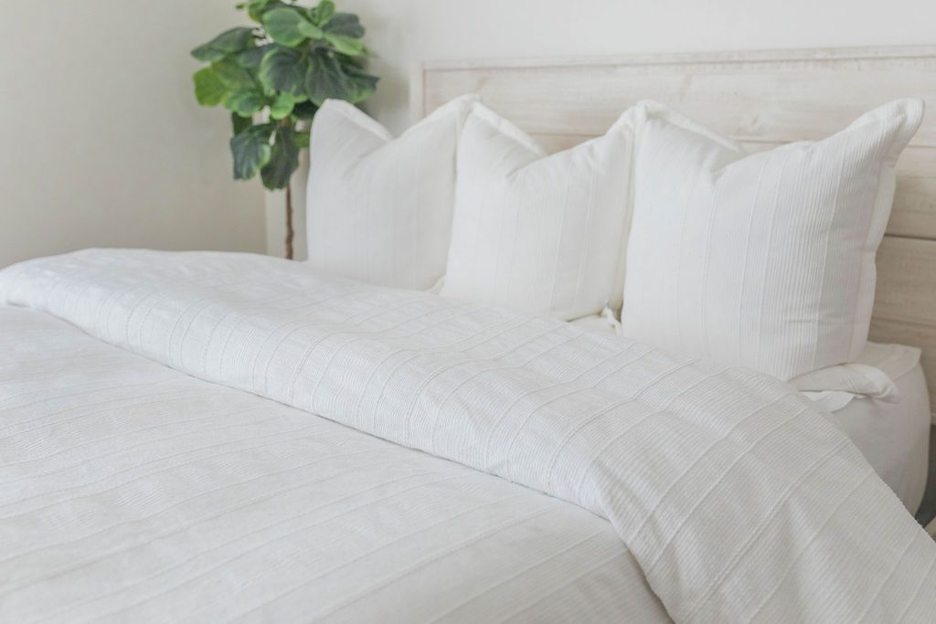 A view of a bed made with white zipper sheets and a white textured zipper duvet as well as some matching large pillows.