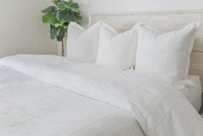 A view of a bed made with white zipper sheets and a white textured zipper duvet as well as some matching large pillows.
