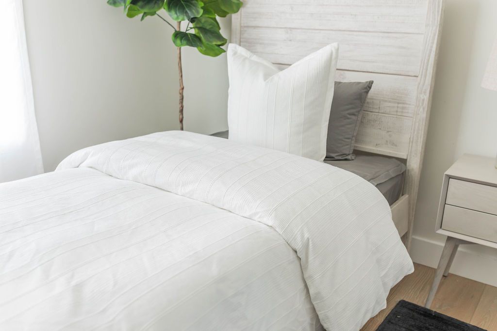 A twin bed made with gray zipper sheets and a white textured zipper duvet folded half way down the bed and adorned with neutral pillows.