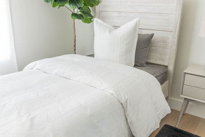 A twin bed made with gray zipper sheets and a white textured zipper duvet folded half way down the bed and adorned with neutral pillows.