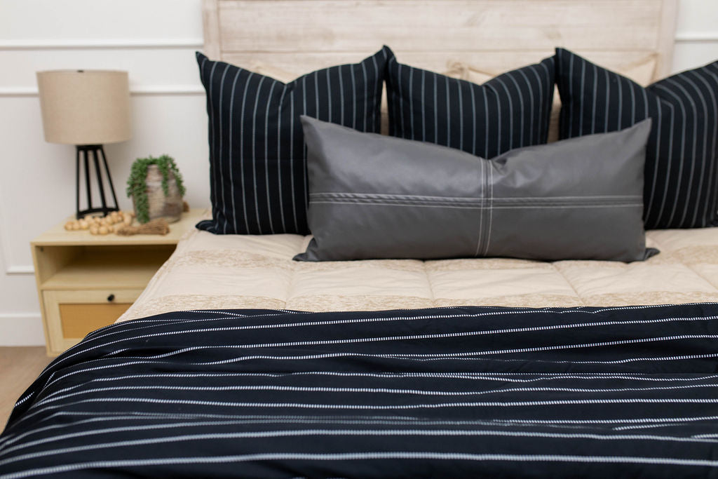 A bed made with tan striped zipper bedding and an assortment of neutral black striped throw pillows and blanket.