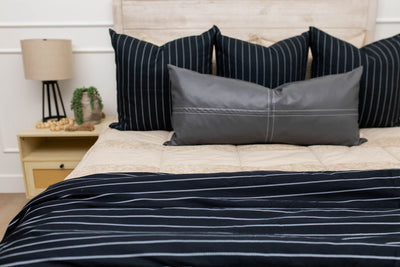 A bed made with tan striped zipper bedding and an assortment of neutral black striped throw pillows and blanket.