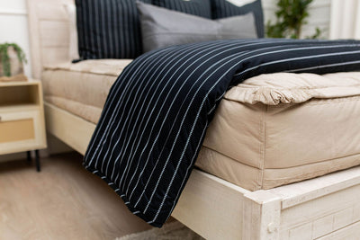 A side view of a bed made with tan striped zipper bedding with a black and white striped blanket folded over the end of the bed.