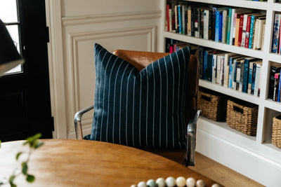 A black striped euro pillow arranged on a leather chair by a table.