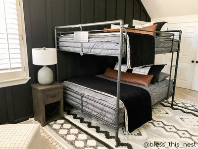 A standard bunk bed with both bunks made with dark charcoal gray zipper bedding and neutral and black pillows and blankets.