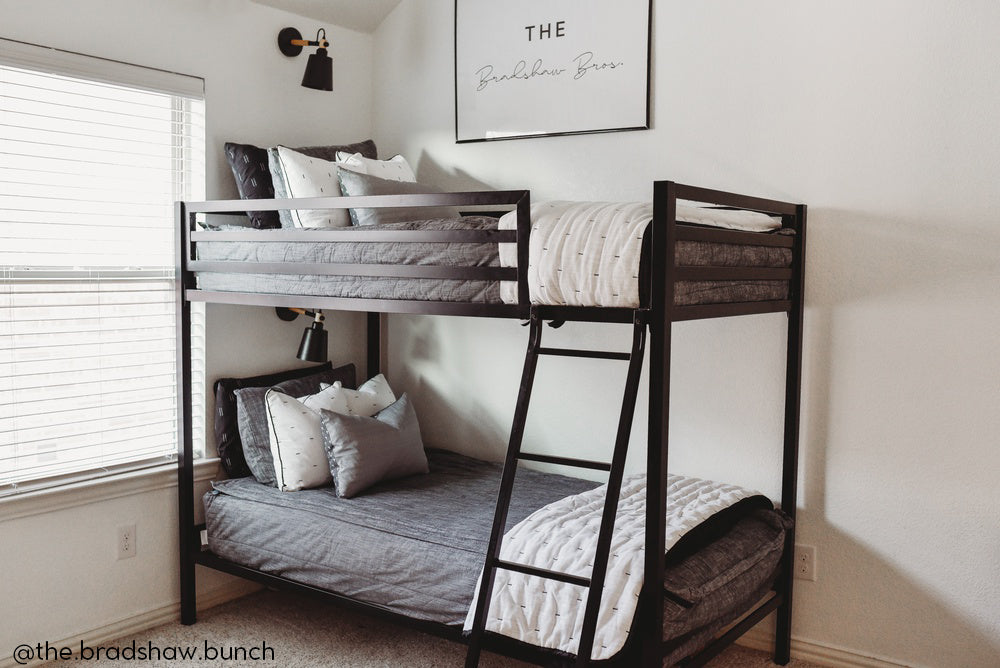 A standard bunk bed with both bunks made with dark charcoal gray zipper bedding and white and black pattern pillows and blankets.