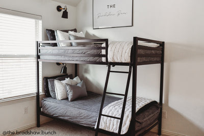 A standard bunk bed with both bunks made with dark charcoal gray zipper bedding and white and black pattern pillows and blankets.