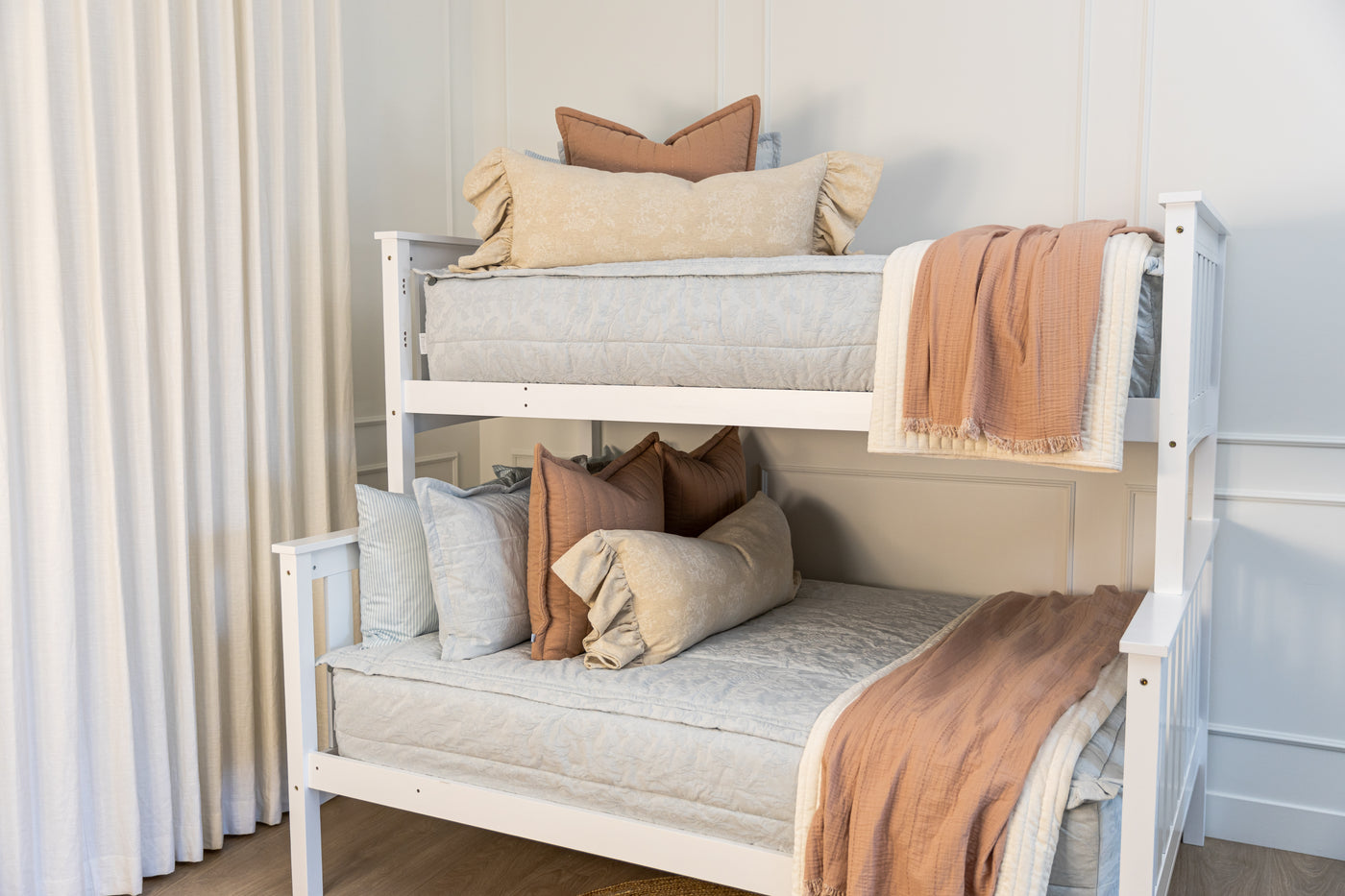 A bunk bed made with light blue floral embossed zipper bedding with cream and terracotta accessories