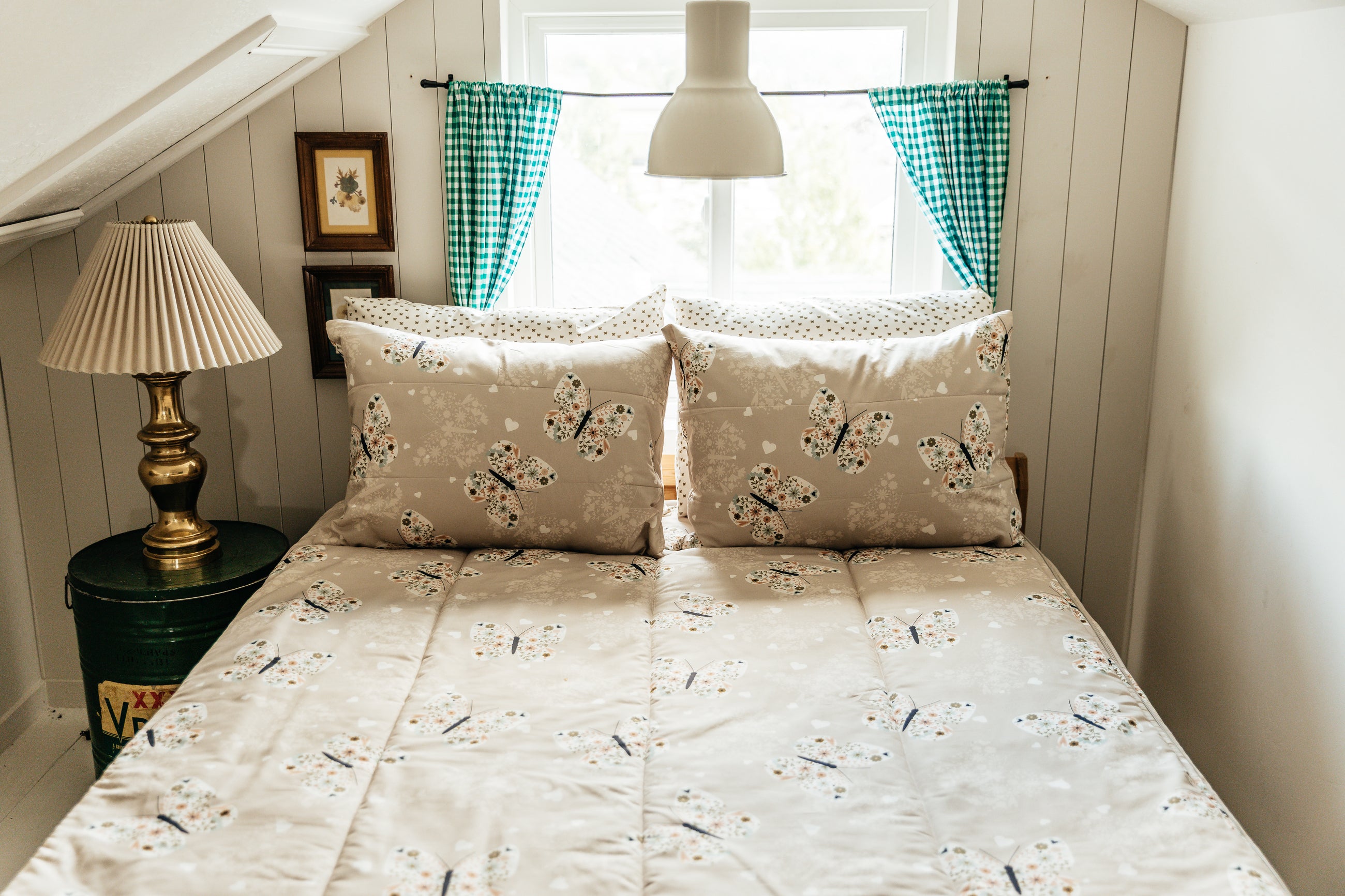 A full size bed made with butterfly zipper bedding, the window behind the bed covered with green gingham curtians.