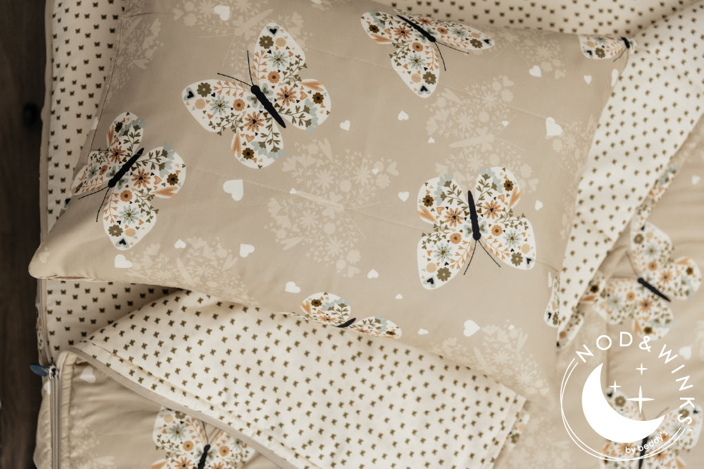 Butterfly printed kids zipper bedding with the top unzipped and one side pulled back to reveal the inside linine, the pillow tossed on top of the bed.