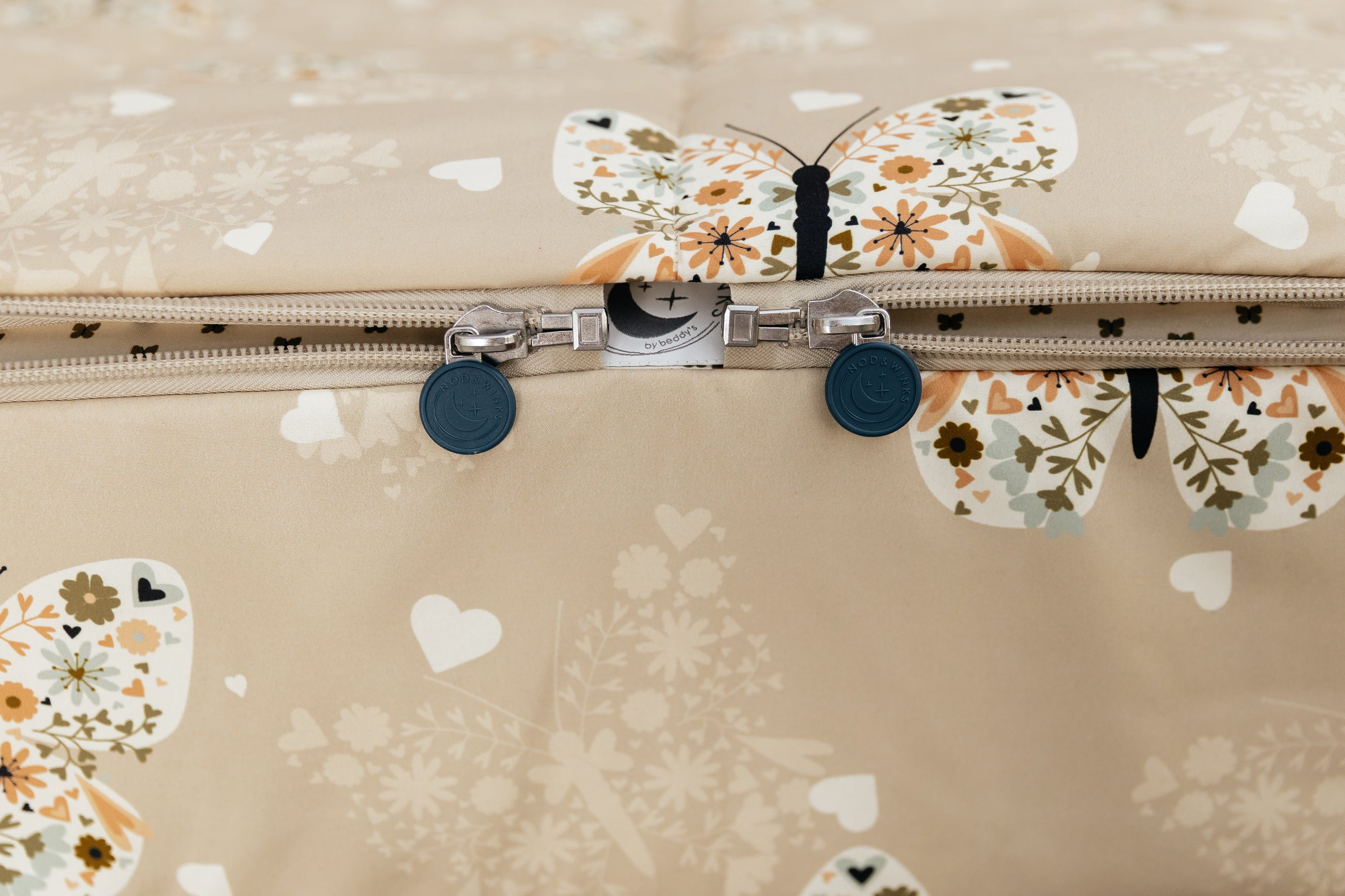 A shot of the two zippers on a set of butterfly printed zipper bedding, the zippers completely unzipped to show how they meet at the foot of the bed.
