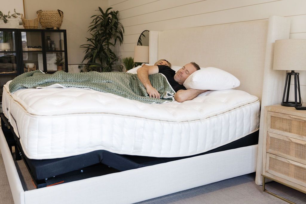 A man and a woman laying together in a bed on an adjustable base with the head and foot of the bed slightly raised.