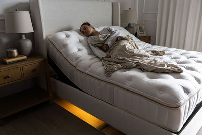 A woman asleep on a mattress positioned on an adjustable base with the head of the base slightly elevated.