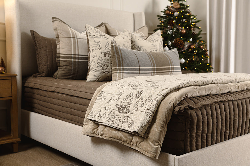 A cream and brown quilted holiday blanket  on brown quilted bedding.