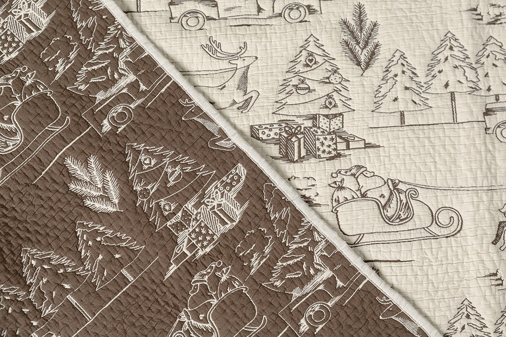 A flat lay of a cream and brown quilted holiday themed blanket.