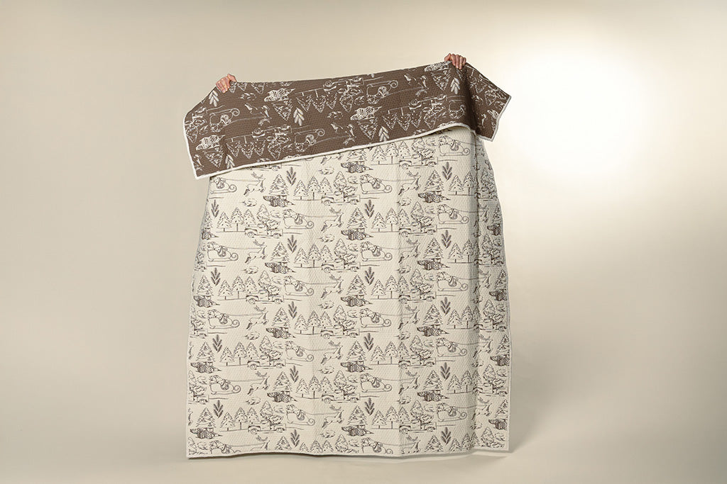 A cream and brown quilted holiday blanket on a paper backdrop.