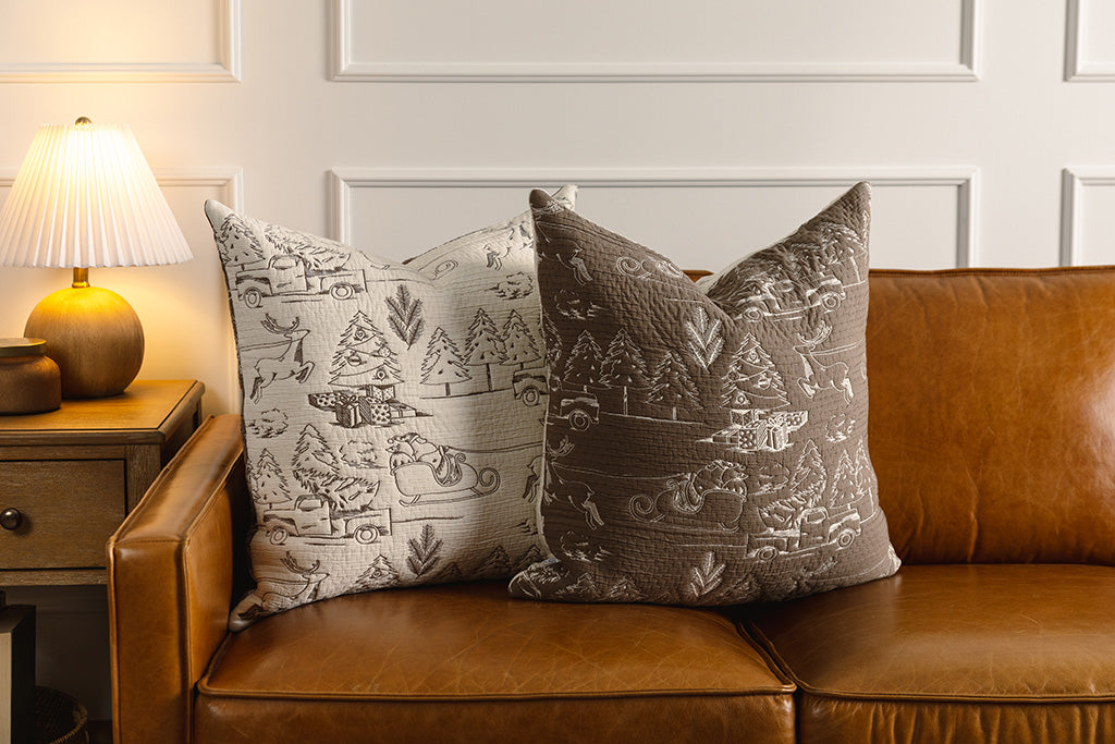 Brown and cream quilted holiday themed pillows on an orange leather couch.