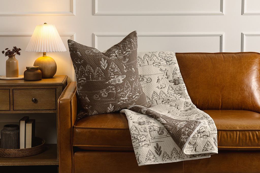 Brown and cream quilted holiday themed pillow and blanket on an orange leather couch.