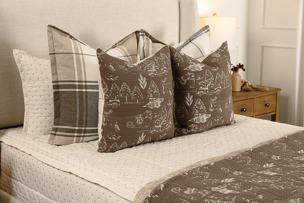 Brown and cream quilted holiday themed pillows and blanket on white stitched bedding.