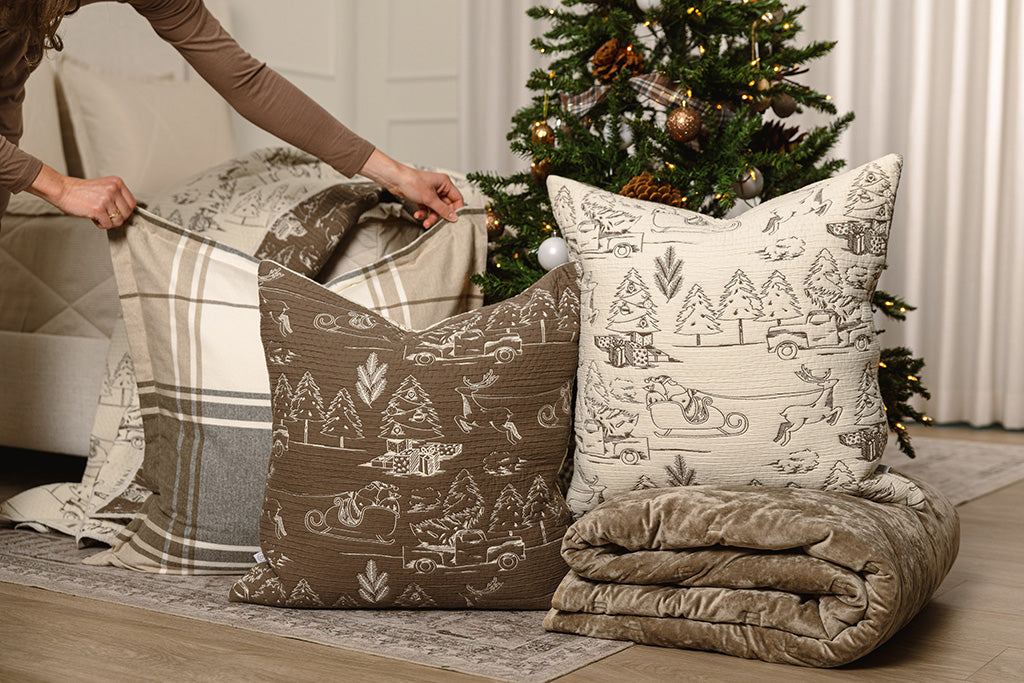 Brown and cream quilted holiday themed pillows with brown, tan, and white accessories next to a Christmas tree.