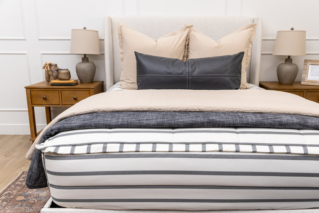 A queen bed made with white and black striped zipper bedding paired with neutral and black accessories.