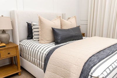 A queen bed made with white and black striped zipper bedding paired with neutral and black accessories.